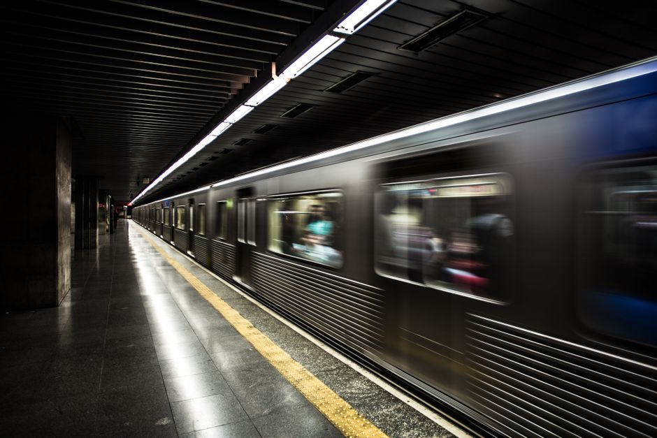 View of a modern underground station platform framed by an oval window, featuring a wall clad in warm-toned wooden panels arranged in a rectangular pattern. The platform surface appears smooth and cle